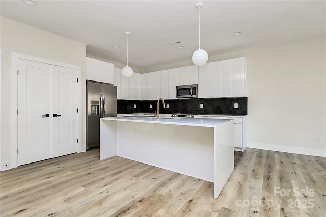 kitchen with white cabinetry, decorative light fixtures, stainless steel appliances, and an island with sink