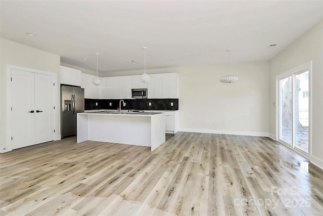 kitchen with pendant lighting, appliances with stainless steel finishes, white cabinetry, backsplash, and a center island with sink