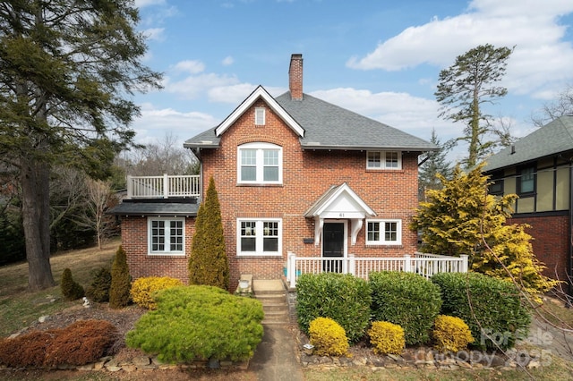 view of front of home featuring a balcony, roof with shingles, a chimney, and brick siding