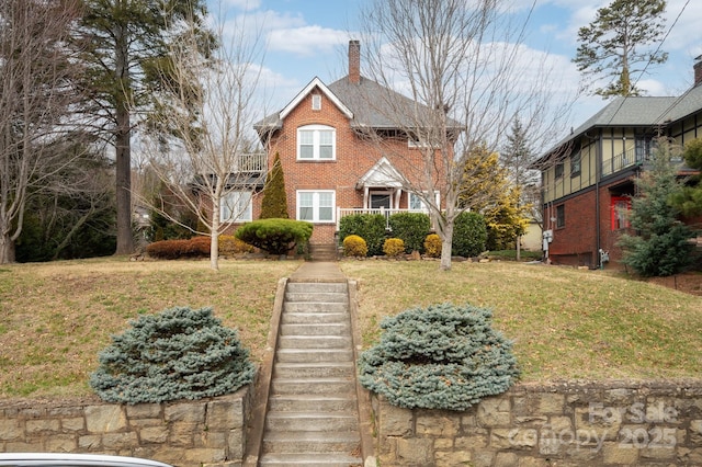 view of front of house with stairway, brick siding, a front yard, and a chimney