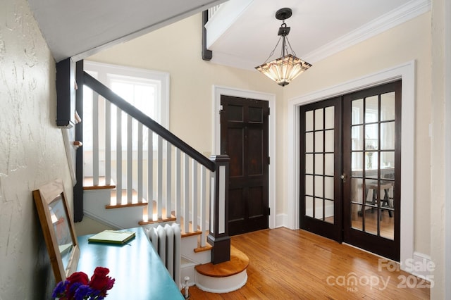 entrance foyer featuring radiator heating unit, ornamental molding, wood finished floors, stairs, and french doors