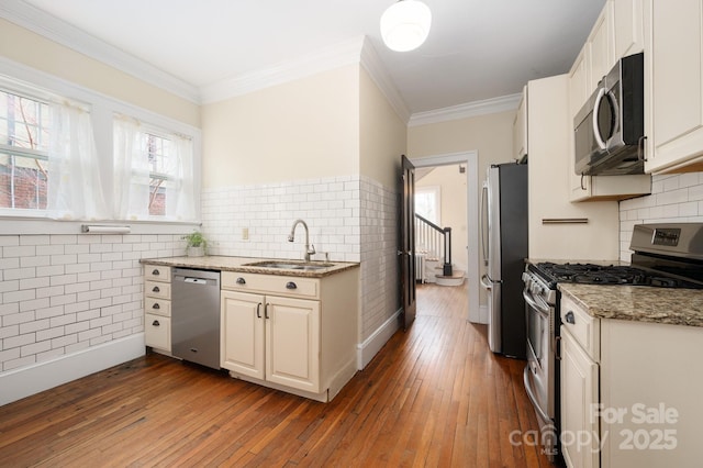 kitchen with appliances with stainless steel finishes, light stone countertops, crown molding, light wood-style floors, and a sink