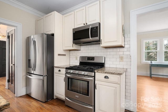 kitchen with white cabinets, light stone countertops, stainless steel appliances, and crown molding