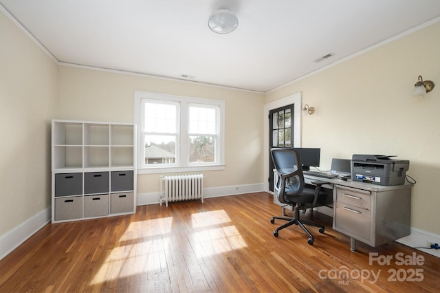 office space with wood finished floors, baseboards, ornamental molding, visible vents, and radiator