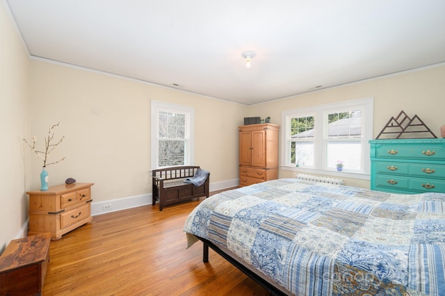 bedroom with radiator, light wood finished floors, baseboards, and ornamental molding