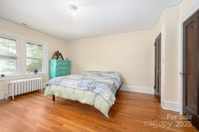 bedroom featuring radiator heating unit, crown molding, baseboards, and wood finished floors