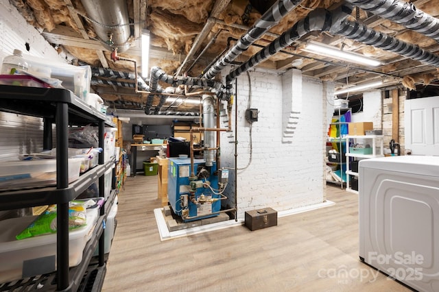 unfinished basement featuring light wood-style flooring, brick wall, a heating unit, and washer / dryer