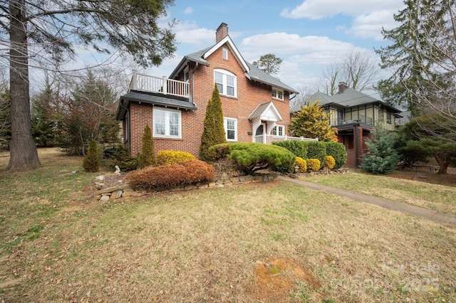 traditional-style house featuring a balcony, a chimney, a front lawn, and brick siding