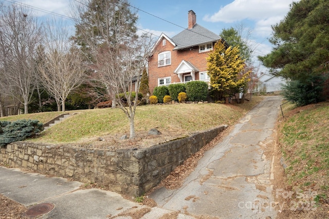 colonial-style house featuring a front lawn, a chimney, and brick siding