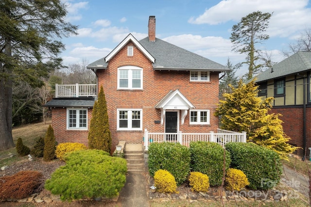 view of front of property with a balcony, brick siding, a shingled roof, and a chimney