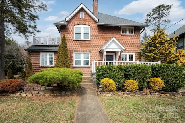 view of front of home featuring a front yard, a balcony, a chimney, and brick siding