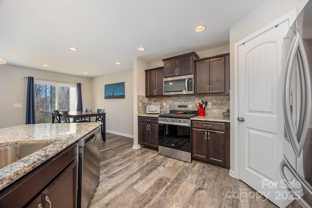 kitchen with stainless steel appliances, dark brown cabinets, light hardwood / wood-style floors, and decorative backsplash