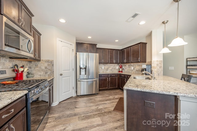 kitchen featuring appliances with stainless steel finishes, decorative light fixtures, sink, light hardwood / wood-style floors, and kitchen peninsula