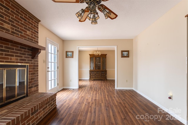 unfurnished living room with ceiling fan, dark hardwood / wood-style floors, a brick fireplace, and a textured ceiling