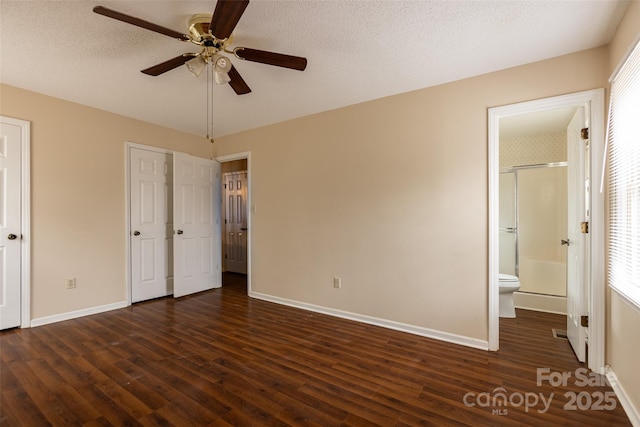 unfurnished bedroom with ensuite bath, dark wood-type flooring, ceiling fan, a textured ceiling, and multiple closets