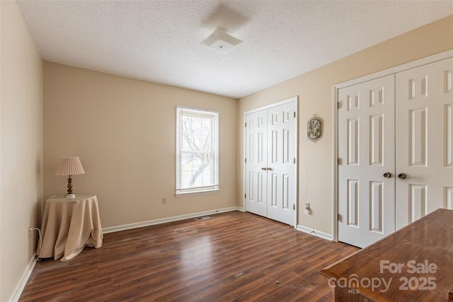 unfurnished bedroom with a textured ceiling, dark wood-type flooring, and multiple closets