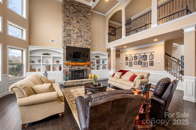 living room featuring built in features, a towering ceiling, decorative columns, a fireplace, and dark hardwood / wood-style flooring