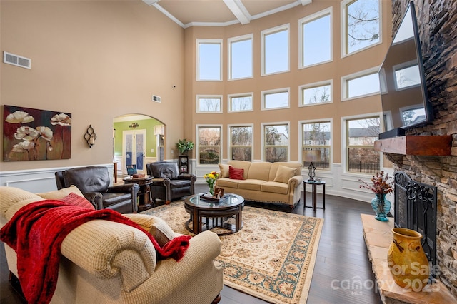 living room with ornamental molding, a stone fireplace, dark hardwood / wood-style floors, and beam ceiling