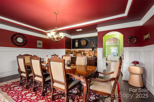 dining space featuring wood-type flooring, ornamental molding, a raised ceiling, and a chandelier