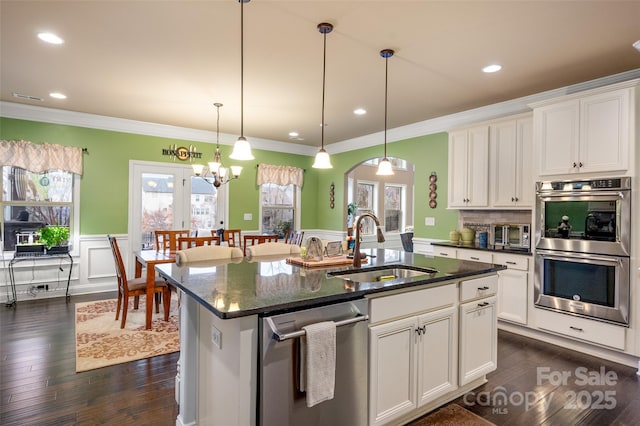 kitchen with sink, white cabinetry, hanging light fixtures, appliances with stainless steel finishes, and an island with sink