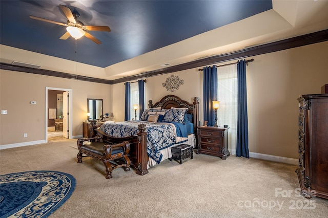 carpeted bedroom with a tray ceiling, ornamental molding, ceiling fan, and ensuite bathroom