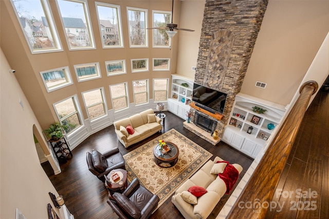 living room featuring dark hardwood / wood-style floors, plenty of natural light, a stone fireplace, and a high ceiling