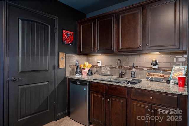 kitchen featuring sink, light stone counters, dishwashing machine, and dark brown cabinetry