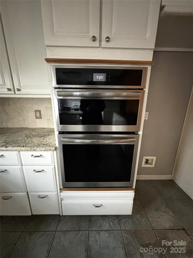 kitchen with double oven, light stone counters, white cabinets, and decorative backsplash