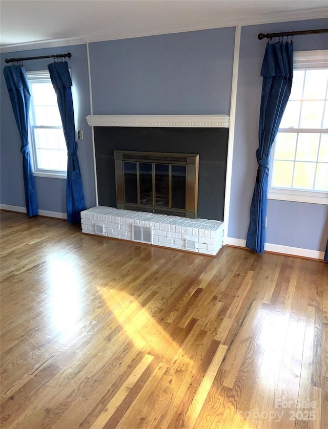 unfurnished living room featuring a brick fireplace, wood finished floors, visible vents, and baseboards