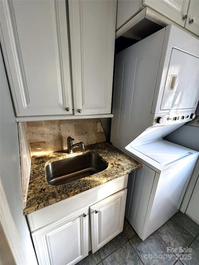 laundry area featuring cabinet space, a sink, and stacked washer / drying machine