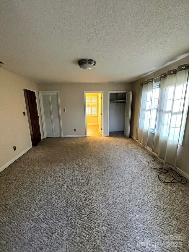 unfurnished bedroom featuring a textured ceiling, multiple closets, carpet flooring, and baseboards