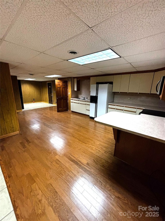 interior space featuring white fridge with ice dispenser, light countertops, a drop ceiling, and light wood-style floors