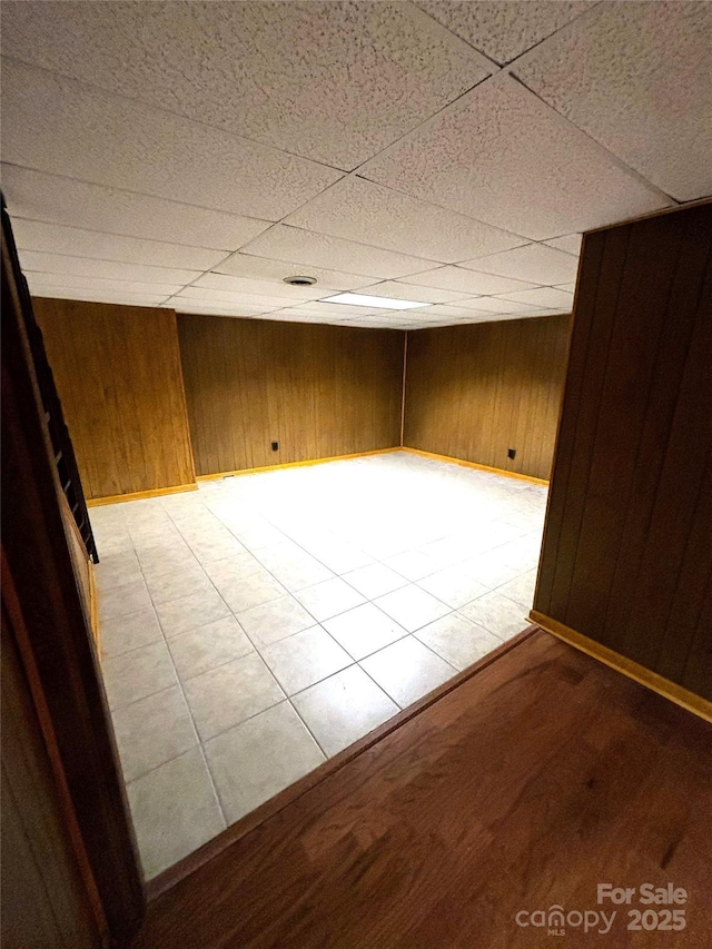 spare room featuring a paneled ceiling, wooden walls, and baseboards