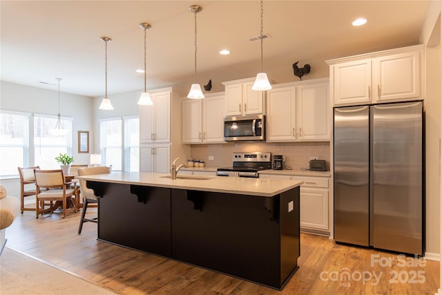 kitchen featuring decorative backsplash, a kitchen breakfast bar, stainless steel appliances, light countertops, and light wood-style floors