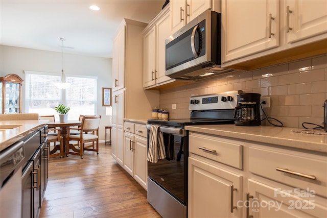 kitchen featuring light wood finished floors, tasteful backsplash, appliances with stainless steel finishes, light stone counters, and hanging light fixtures