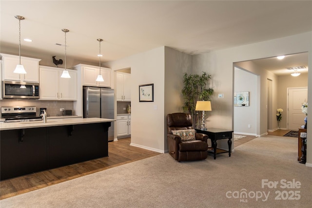 kitchen featuring appliances with stainless steel finishes, light countertops, carpet flooring, a kitchen bar, and white cabinetry