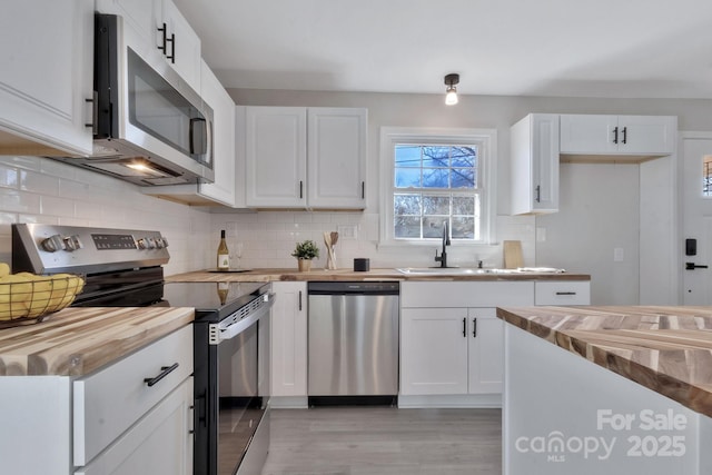 kitchen featuring wooden counters, appliances with stainless steel finishes, a sink, and white cabinetry