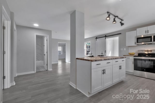 kitchen featuring a barn door, stainless steel appliances, white cabinetry, light wood-style floors, and decorative backsplash