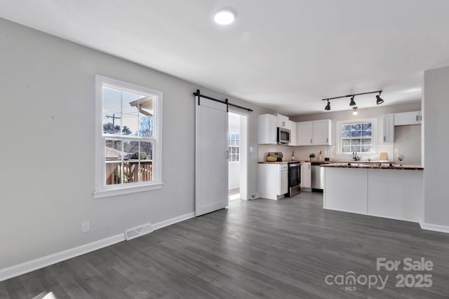 unfurnished living room with a healthy amount of sunlight, a barn door, visible vents, and dark wood-type flooring