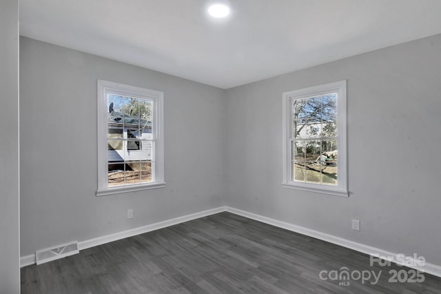 spare room with dark wood-style flooring, visible vents, and baseboards