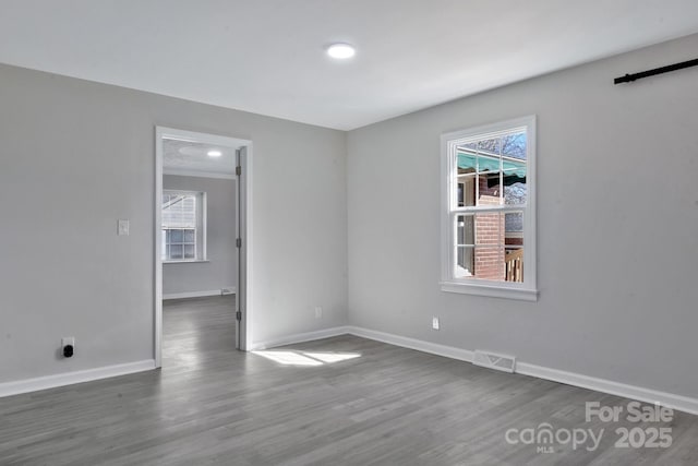 spare room with dark wood-style flooring, plenty of natural light, and visible vents