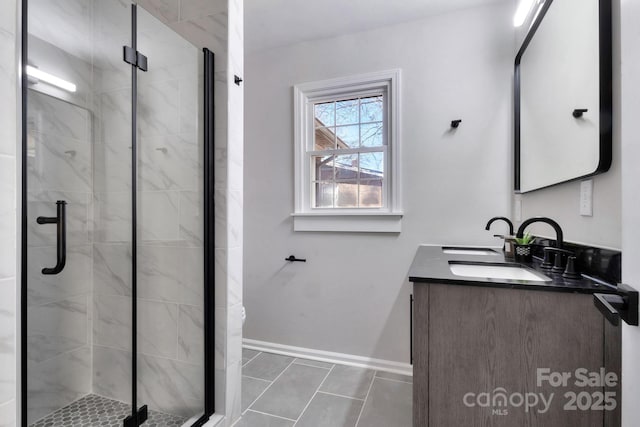 full bathroom featuring a sink, double vanity, a shower stall, and baseboards