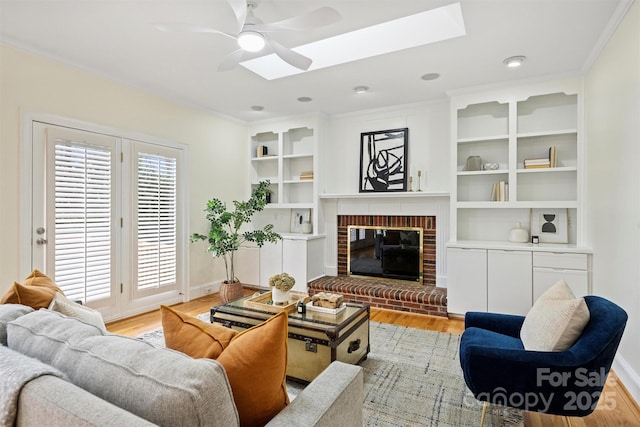 living room featuring crown molding, ceiling fan, a skylight, light hardwood / wood-style floors, and a brick fireplace