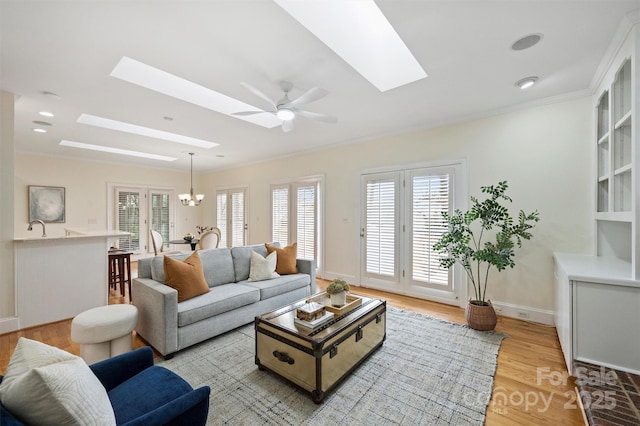 living room with sink, crown molding, a skylight, light wood-type flooring, and ceiling fan with notable chandelier