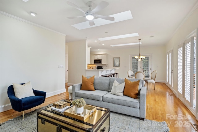 living room featuring crown molding, a skylight, ceiling fan with notable chandelier, and light wood-type flooring