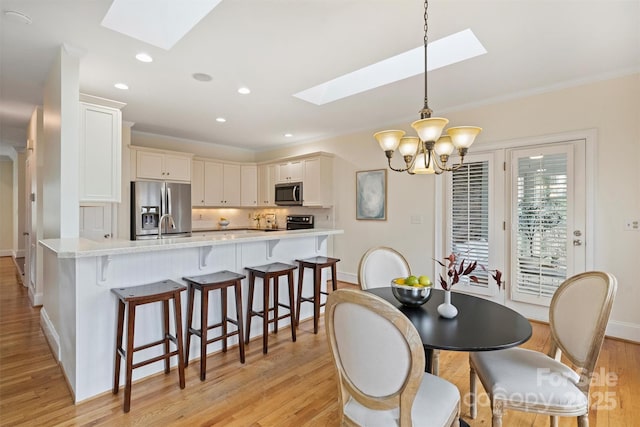 dining area with light hardwood / wood-style flooring, crown molding, a skylight, and a chandelier