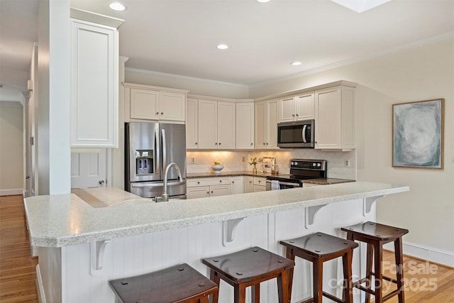 kitchen with light wood-type flooring, ornamental molding, appliances with stainless steel finishes, a kitchen breakfast bar, and decorative backsplash