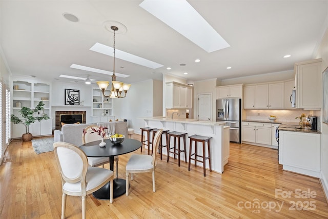 dining room featuring ceiling fan with notable chandelier, light hardwood / wood-style flooring, a fireplace, and a skylight