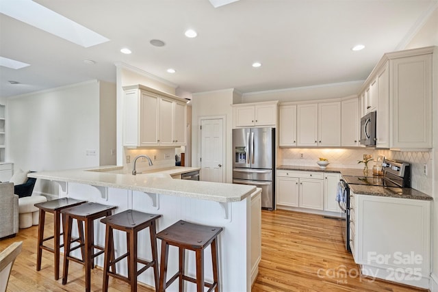 kitchen featuring a skylight, appliances with stainless steel finishes, a kitchen breakfast bar, kitchen peninsula, and backsplash