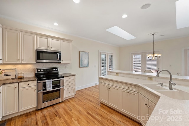 kitchen featuring sink, light hardwood / wood-style flooring, stainless steel appliances, cream cabinets, and decorative light fixtures